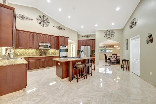 kitchen with a kitchen island, appliances with stainless steel finishes, a kitchen breakfast bar, ornamental molding, and light stone counters