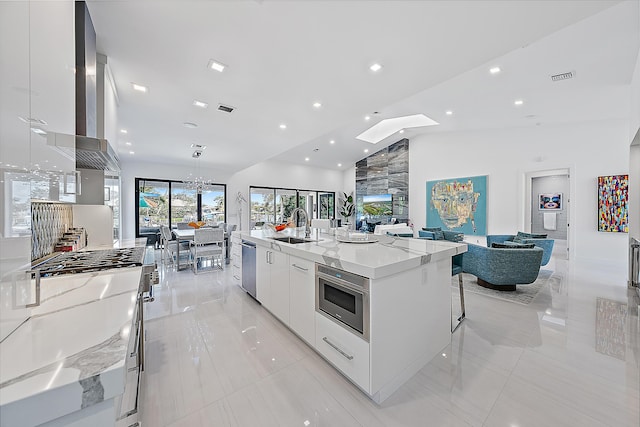 kitchen featuring sink, light stone countertops, white cabinets, stainless steel dishwasher, and a large island with sink