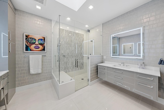 bathroom with a shower with shower door, a skylight, tile walls, vanity, and tile patterned flooring