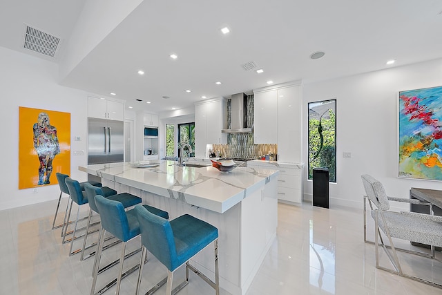 kitchen featuring wall chimney exhaust hood, a kitchen bar, stainless steel appliances, a large island, and white cabinets