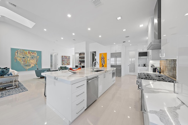 kitchen with sink, appliances with stainless steel finishes, white cabinetry, light stone counters, and a large island with sink