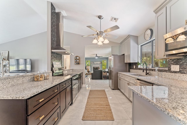 kitchen featuring sink, appliances with stainless steel finishes, dark brown cabinets, light stone countertops, and wall chimney exhaust hood