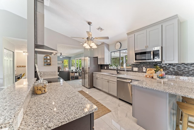 kitchen with sink, a kitchen breakfast bar, stainless steel appliances, light stone countertops, and wall chimney exhaust hood