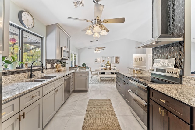 kitchen with wall chimney exhaust hood, lofted ceiling, sink, gray cabinetry, and stainless steel appliances