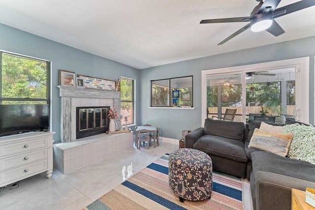 living room featuring ceiling fan, light tile patterned floors, a tile fireplace, and a wealth of natural light