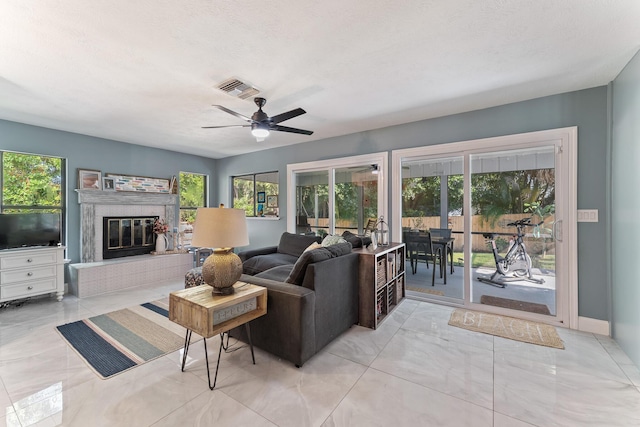 living room featuring ceiling fan, a fireplace, and a textured ceiling