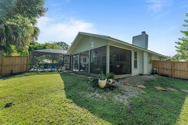 back of house featuring ceiling fan, a sunroom, a yard, and glass enclosure