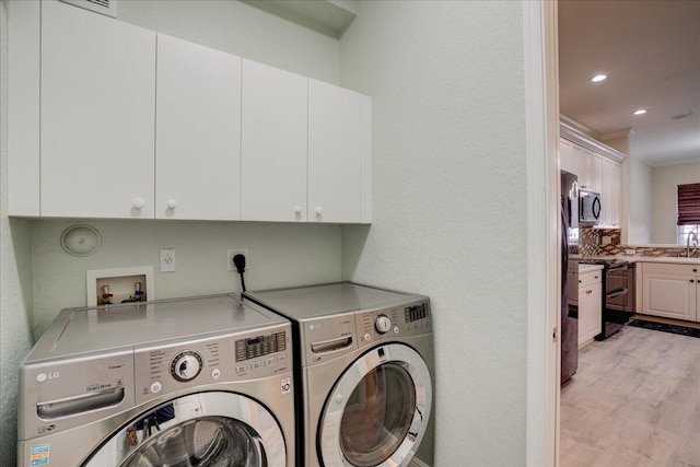 laundry room with cabinet space, a textured wall, crown molding, washer and dryer, and light wood-type flooring