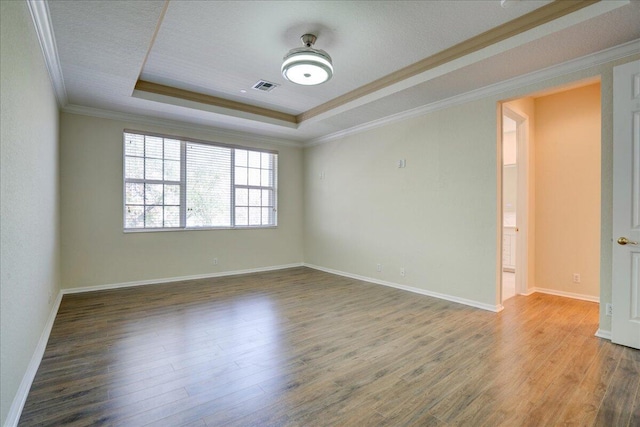 empty room featuring wood finished floors, visible vents, baseboards, ornamental molding, and a raised ceiling