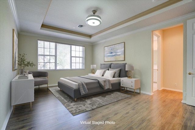 bedroom with wood finished floors, visible vents, baseboards, a raised ceiling, and crown molding