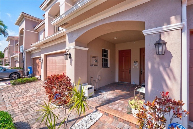 view of exterior entry with decorative driveway, an attached garage, and stucco siding