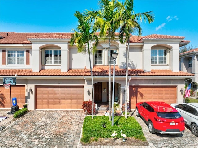 mediterranean / spanish-style home featuring a garage, decorative driveway, a tile roof, and stucco siding