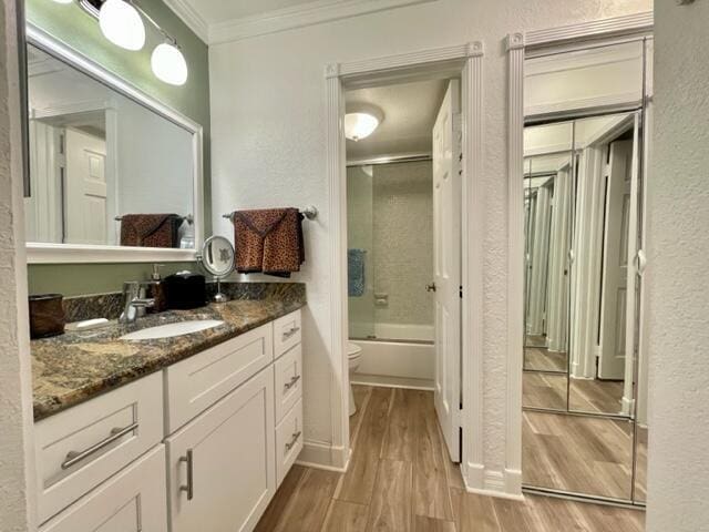 full bathroom with hardwood / wood-style floors, enclosed tub / shower combo, vanity, ornamental molding, and toilet