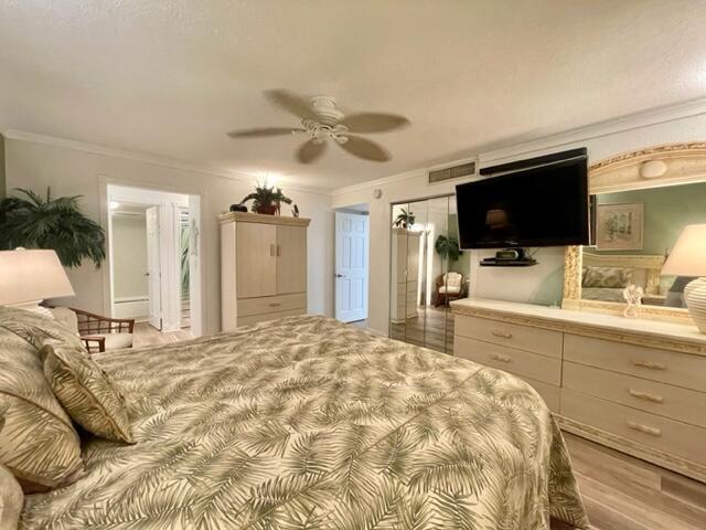 bedroom featuring ornamental molding, ensuite bathroom, ceiling fan, and light wood-type flooring