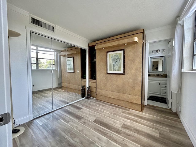unfurnished bedroom with hardwood / wood-style flooring, ornamental molding, connected bathroom, and a closet