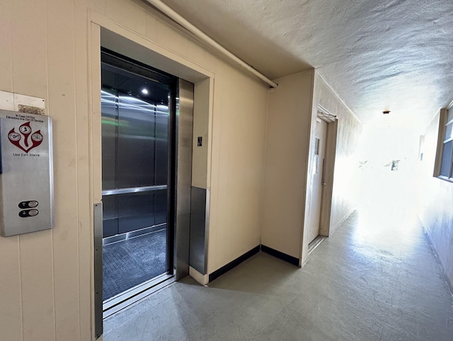 corridor with elevator and a textured ceiling
