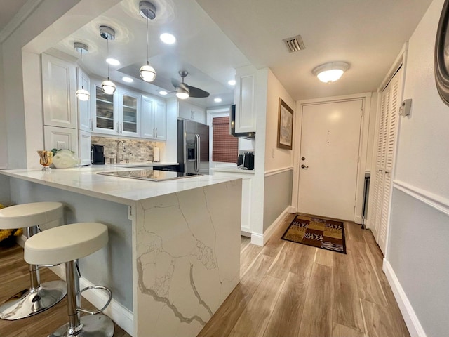 kitchen featuring a breakfast bar area, white cabinetry, decorative light fixtures, stainless steel fridge with ice dispenser, and kitchen peninsula