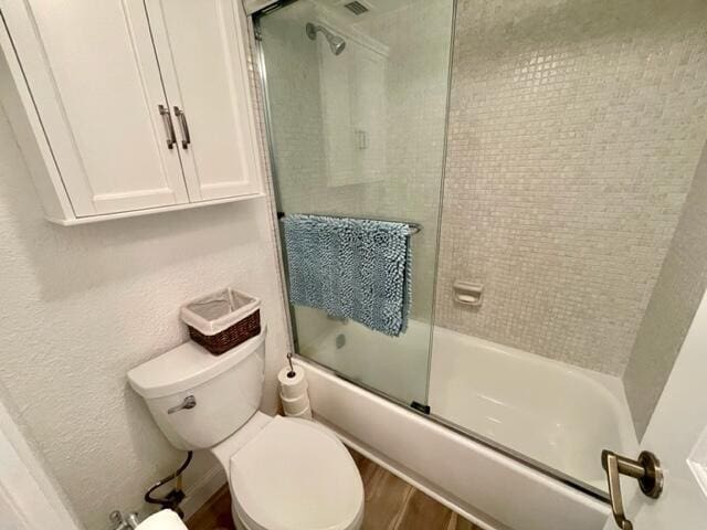 bathroom with bath / shower combo with glass door, toilet, and wood-type flooring