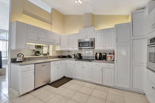 kitchen with light tile patterned floors, high vaulted ceiling, white cabinets, appliances with stainless steel finishes, and tasteful backsplash