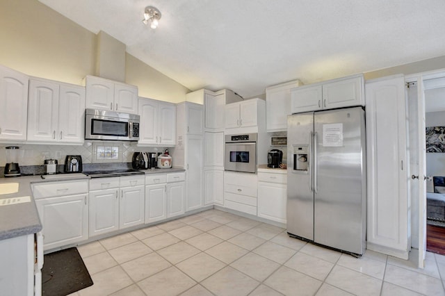 kitchen with tasteful backsplash, lofted ceiling, appliances with stainless steel finishes, white cabinets, and light tile patterned flooring