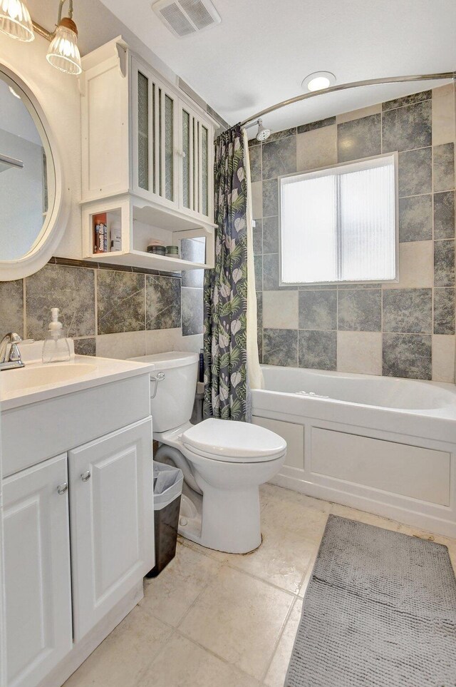 full bathroom featuring toilet, tile walls, vanity, visible vents, and shower / tub combo with curtain