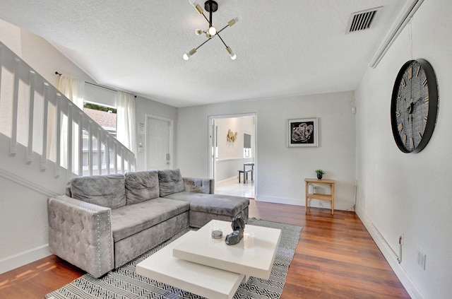 living area featuring a textured ceiling, wood finished floors, visible vents, baseboards, and stairway