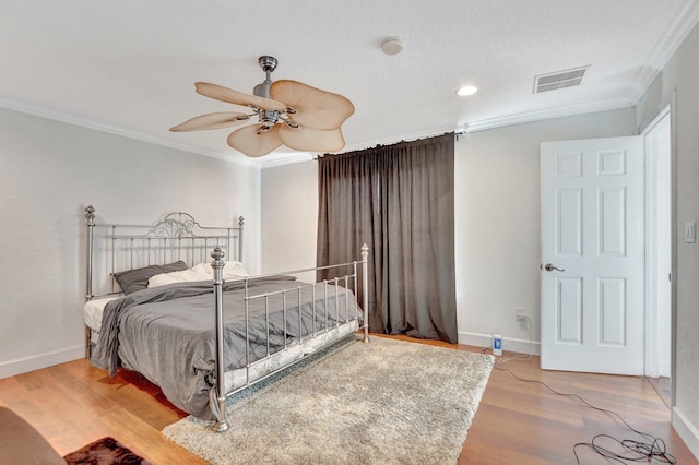 bedroom with visible vents, crown molding, baseboards, and wood finished floors