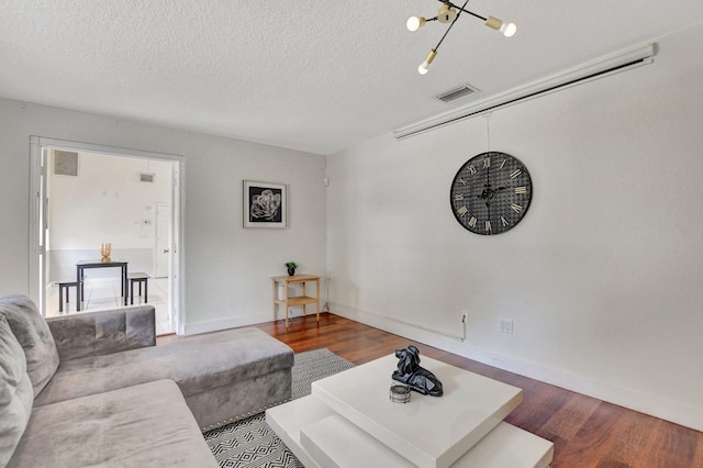 living room with baseboards, a textured ceiling, visible vents, and wood finished floors