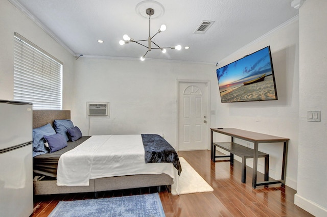 bedroom featuring a wall unit AC, visible vents, ornamental molding, freestanding refrigerator, and wood finished floors