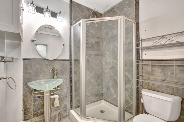 bathroom with a stall shower, a sink, toilet, and tile walls