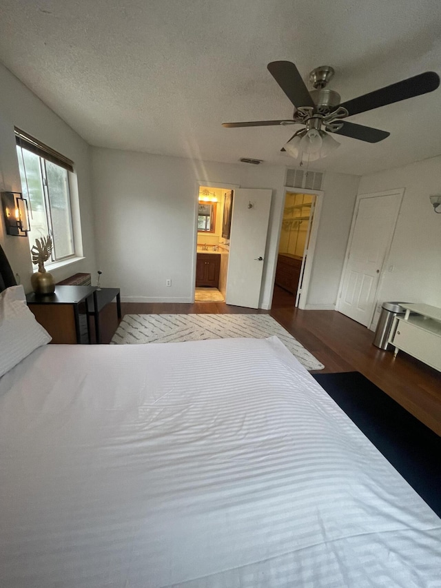 bedroom with visible vents, ceiling fan, connected bathroom, a textured ceiling, and wood finished floors