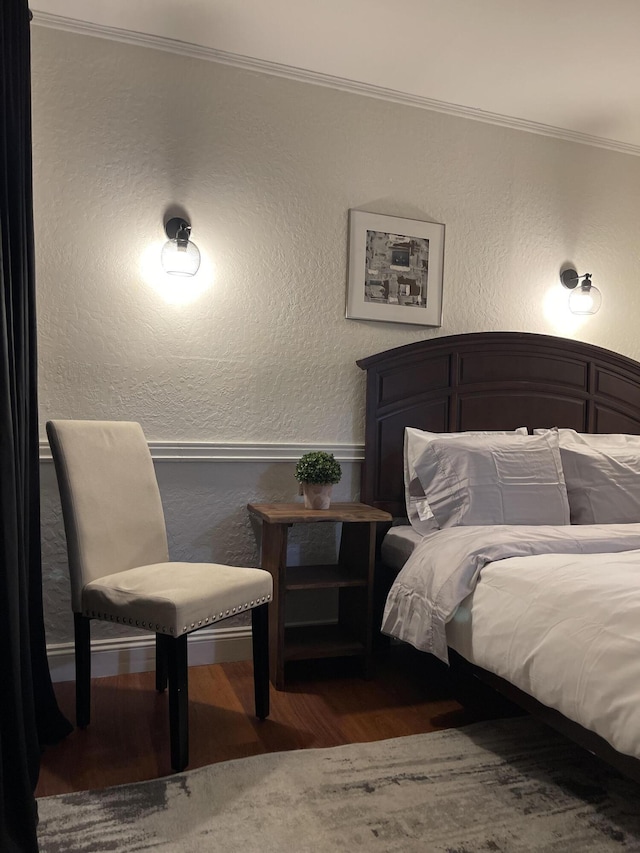 bedroom with ornamental molding, a textured wall, and wood finished floors