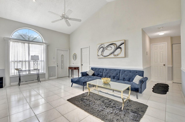 living room with a ceiling fan, a textured ceiling, high vaulted ceiling, baseboards, and tile patterned floors