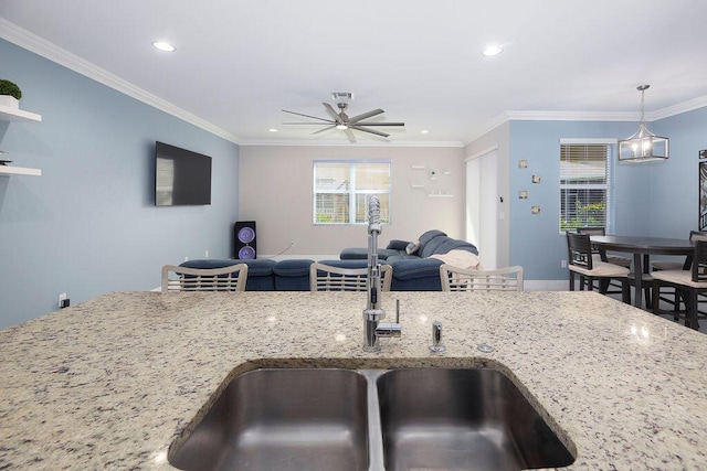 kitchen featuring light stone counters, sink, crown molding, and decorative light fixtures