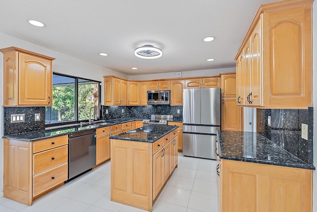 kitchen with appliances with stainless steel finishes, a sink, dark stone countertops, and light brown cabinetry