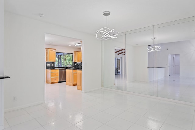 unfurnished dining area featuring a sink, light tile patterned floors, baseboards, and a notable chandelier