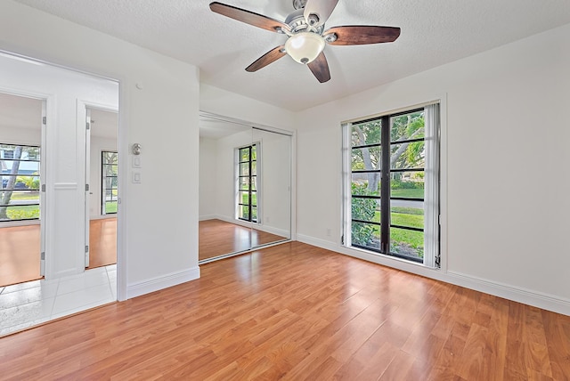 empty room with a ceiling fan, light wood-style flooring, baseboards, and a textured ceiling