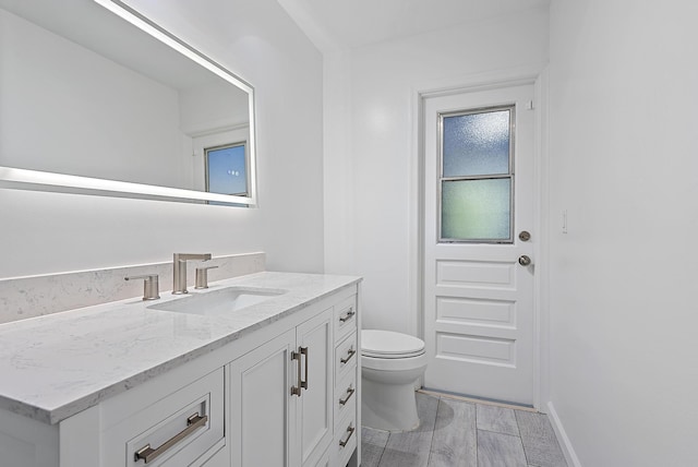 half bathroom featuring baseboards, vanity, toilet, and wood finished floors