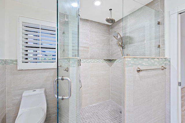 bathroom with tile walls, a shower stall, and toilet