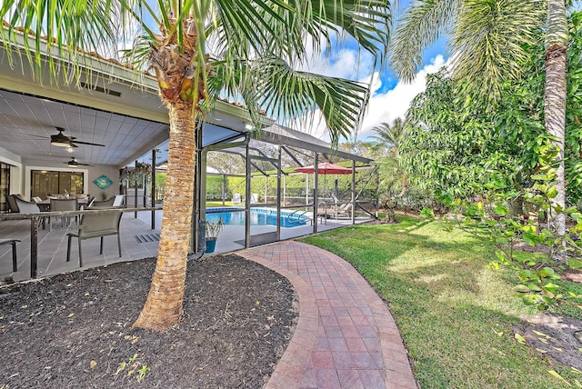 view of yard featuring glass enclosure, an outdoor pool, a patio area, and ceiling fan