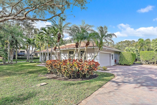 view of front of property featuring a tiled roof, an attached garage, decorative driveway, a front yard, and stucco siding