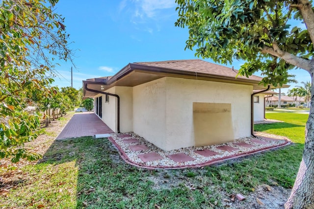 view of home's exterior with roof with shingles, a lawn, a patio area, and stucco siding