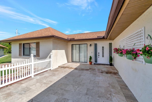 doorway to property featuring a shingled roof, stucco siding, fence, and a patio