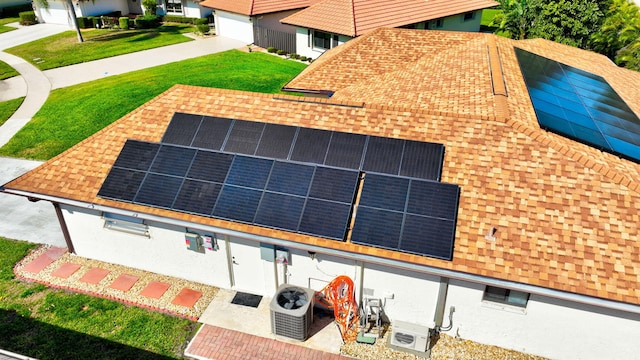 exterior space with a shingled roof, ac unit, a yard, and solar panels