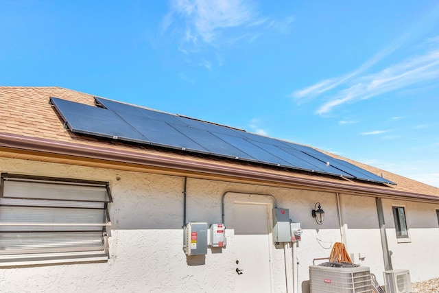 view of side of home featuring solar panels, a shingled roof, stucco siding, and central air condition unit