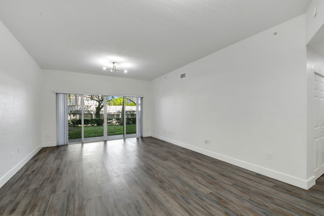 empty room featuring a textured ceiling, dark wood-type flooring, visible vents, and baseboards