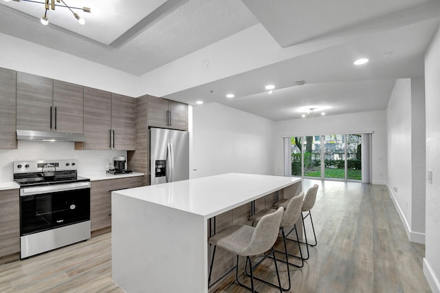 kitchen with modern cabinets, appliances with stainless steel finishes, a kitchen breakfast bar, light wood-type flooring, and under cabinet range hood