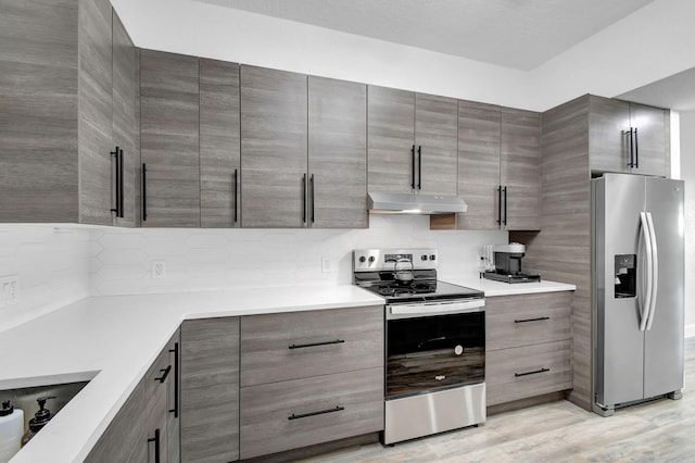 kitchen featuring stainless steel appliances, backsplash, light countertops, and under cabinet range hood