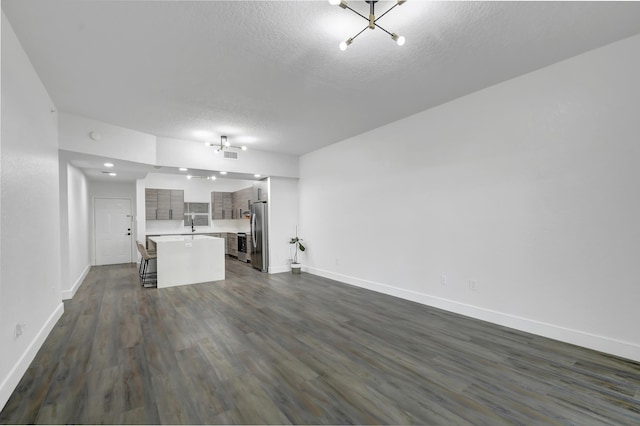 unfurnished living room featuring a textured ceiling, dark wood finished floors, and baseboards