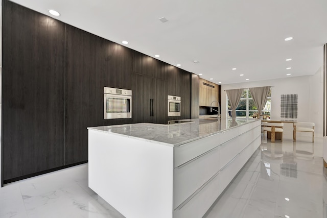 kitchen with white cabinetry, a spacious island, oven, and light stone countertops